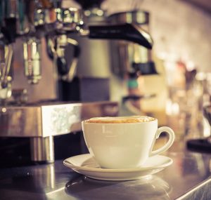 Expresso maker with cappuccino in coffee cup on saucer.